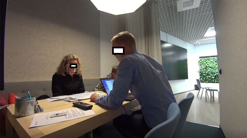 A picture containing three persons around a desk, and a laptop computer on the desk.